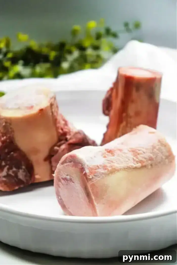 Golden Air-Fried Bone Marrow 4 Three raw beef bones, perfect for air fryer bone marrow, are placed in a white dish. The bones have a light pink hue with some white marbling and fat visible. They are situated in a well-lit setting with green foliage blurred in the background.