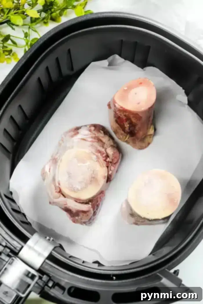 Golden Air-Fried Bone Marrow 5 Juicy beef marrow bones rest on parchment paper inside an air fryer basket, ready to become a gourmet delight. A few green leaves peek through in the background, hinting at a fresh twist to this classic air fryer bone marrow delicacy.