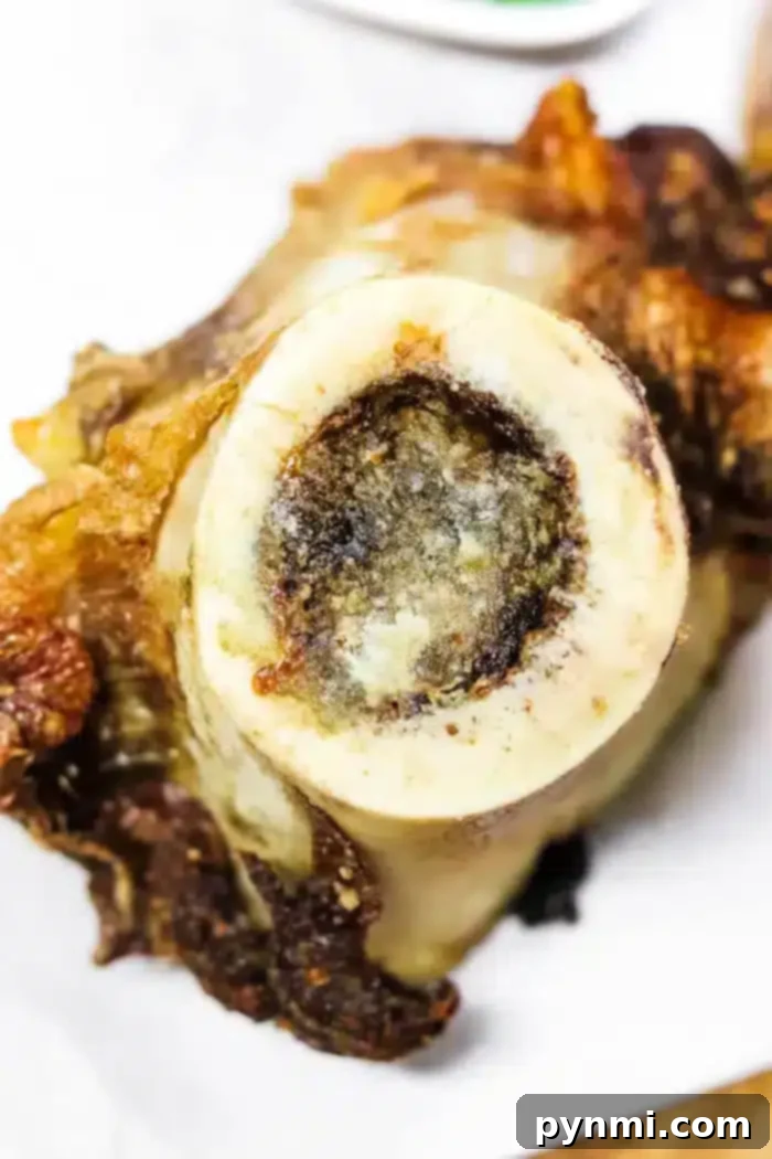 Golden Air-Fried Bone Marrow 6 Close-up of a roasted bone with exposed bone marrow at the center, air fryer crisping its outer edges to perfection. The background is blurred, set against a white surface beneath the bone.