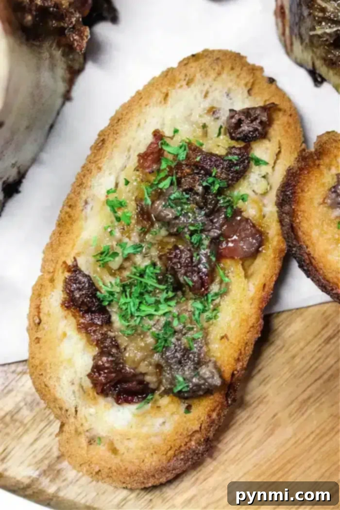Golden Air-Fried Bone Marrow 7 A slice of toasted bread topped with chopped beef and rich bone marrow, garnished with finely chopped parsley, displayed on a wooden surface.