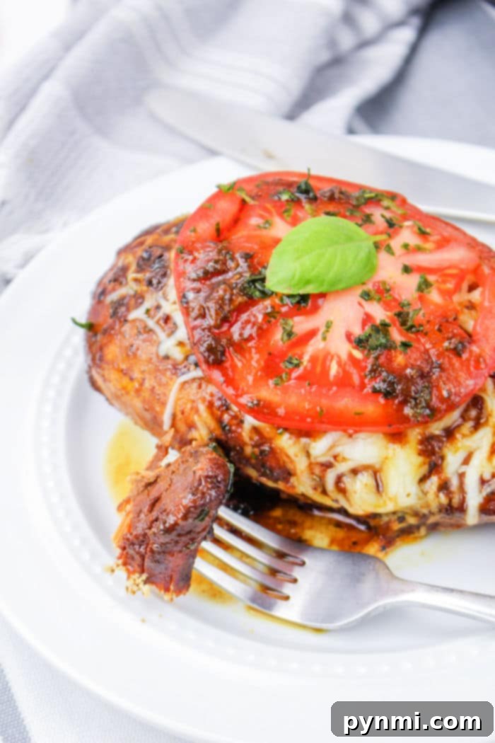 From Freezer to Feast: Slow Cooker Chicken Breasts 6 Crockpot caprese chicken made from frozen breasts is topped with melted cheese, a tomato slice, and fresh basil, all elegantly arranged on a white plate with a fork and knife.
