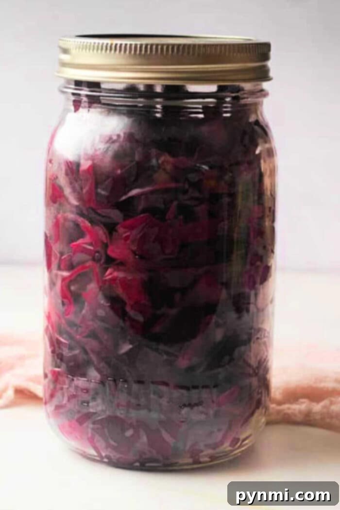 A jar of vibrant purple pickled cabbage with a metal lid rests on a light surface, showcasing its rich color and tangy aroma.