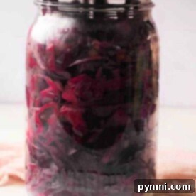 A jar of purple pickled cabbage with a metal lid rests on a light surface, showcasing the vibrant color and tangy aroma reminiscent of a classic pickled red cabbage recipe.