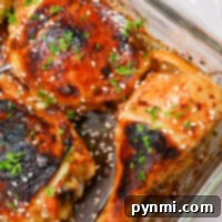 A glass baking dish features Teriyaki chicken drumsticks and thighs, garnished with sesame seeds and chopped herbs. The Cheesecake Factory-inspired chicken pieces are cooked to golden brown perfection with charred areas, and onion slices peek from underneath.