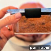A hand holds a glass container filled with seasoned dry rub for pork chops, ready for barbecuing.
