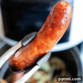 Tongs holding a perfectly cooked sausage, freshly transformed from frozen, in front of an air fryer.