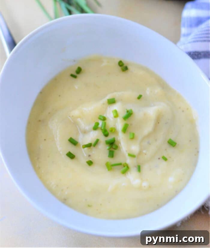 Velvety Instant Pot Potato Leek Comfort 9 A hearty bowl of Potato Leek Soup, garnished with a swirl of cream and fresh chives, captured in a warm, inviting kitchen setting.