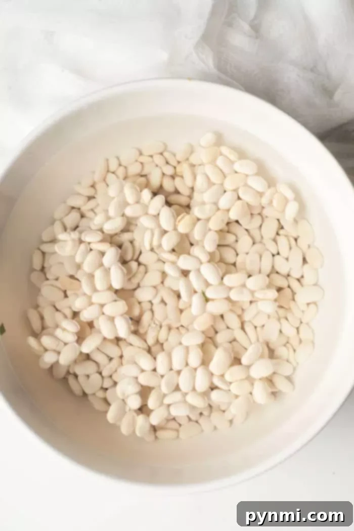 Creamy Northern White Beans 4 A white bowl filled with Great Northern beans and water, actively soaking on a light-colored surface, indicating the start of the rehydration process.