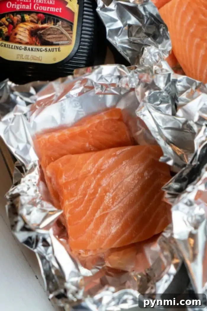 Umami Glazed Salmon Bake 4 Two raw salmon fillets rest on aluminum foil, perfect candidates for becoming oven-baked teriyaki salmon delights. A bottle of original gourmet teriyaki sauce stands in the background, hinting at the delicious transformation awaiting these fillets.