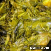Close-up of slow cooker collard greens in a broth, showcasing their glossy texture and rich green color.