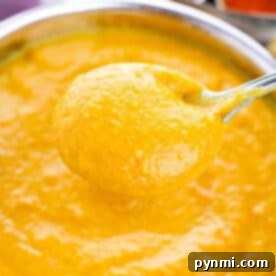 A spoon holding thick, creamy Pumpkin Soup with Canned Pumpkin hovers over a bowl filled with the same golden curry sauce.
