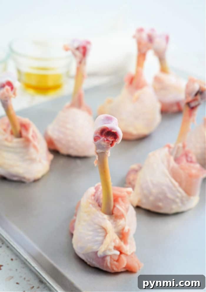 Perfect Lollipop Chicken Drumsticks 4 A top-down view of chicken drumsticks being transformed into lollipops on a cutting board, with the meat pushed down the bone.