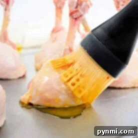 Basting lollipop chicken drumsticks with oil on a baking sheet using a brush.