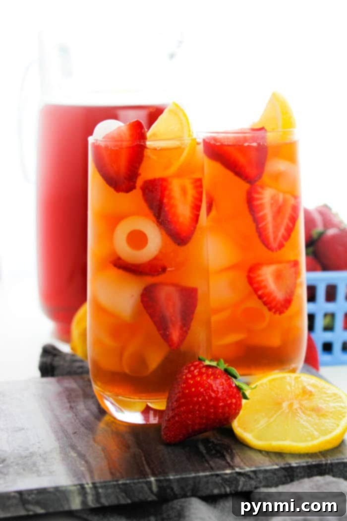 Two glasses of iced strawberry tea with lemon slices, infused with a hint of hibiscus sweet tea, rest on a wooden board.