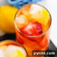 A refreshing glass of hibiscus sweet tea is adorned with lemon and strawberry slices, while lemon slices rest nearby and a basket of strawberries adds a charming touch in the background.