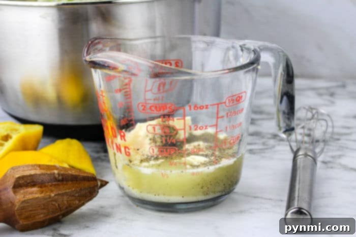 Bold Blue Coleslaw 4 A glass measuring cup with creamy coleslaw dressing, whisk, fresh lemons, and a citrus reamer on a marble surface, ready for making blue cheese coleslaw.