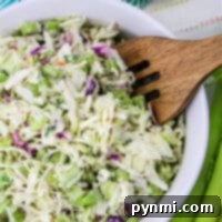 A bowl of blue cheese coleslaw with cabbage and herbs, accompanied by a wooden fork, fresh lemons, and crisp celery on the side.