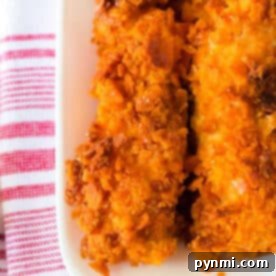 Close-up of crispy Cheese It Chicken Tenders, their orange coating glistening on a white plate, set atop a red and white striped towel.