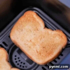 Golden brown and crisp, two slices of toast rest in a black air fryer basket, illustrating the perfection of toasting in an air fryer.