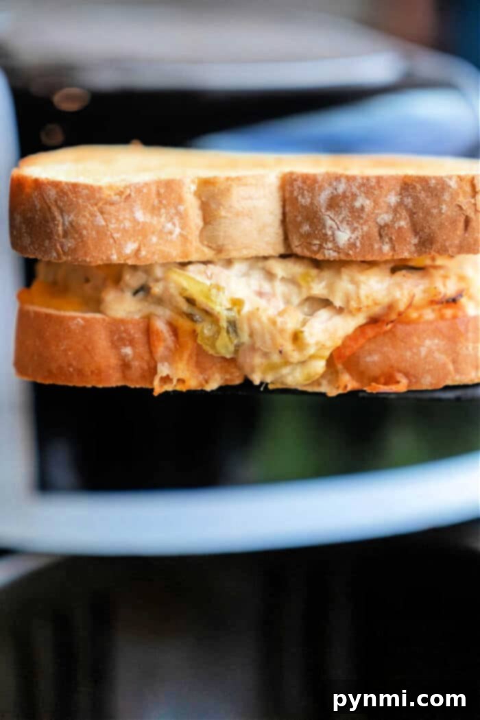 Crispy Air-Fried Tuna Sandwich 2 A close-up of a perfectly toasted air fryer tuna melt. The golden-brown bread has a delightful crunch, revealing a savory, melted cheese and tuna filling peeking from a bitten corner. A truly irresistible and quick lunch or dinner option.
