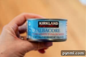 A hand holds a can of Kirkland Signature Albacore Solid White Tuna in Water, thoroughly drained and ready for mixing, an essential first step for any delicious air fryer tuna melt.