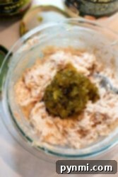 A glass bowl brimming with a creamy, well-mixed tuna salad, featuring visible chunks of tuna and finely chopped pickles, ready to be spread onto bread for a tuna melt.