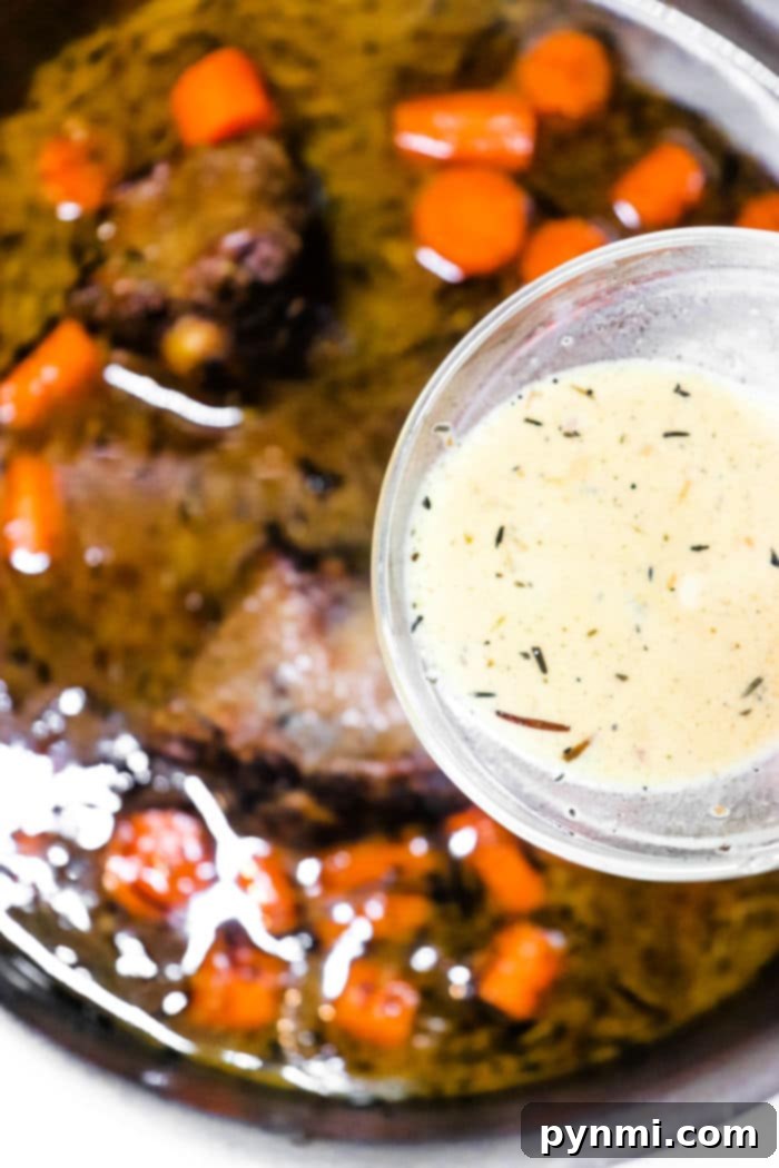 Stovetop Oxtail Perfection 6 A dish with tender, cooked oxtail pieces and sliced carrots in a dark sauce is shown in a pan, reminiscent of how to cook oxtails on the stove. Above the pan, a small glass bowl holds a light creamy sauce speckled with visible herbs.