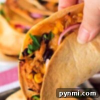 Close-up of a hand holding a taco crafted from air fryer magic, filled with shredded chicken, black beans, corn, cilantro, and red onion.