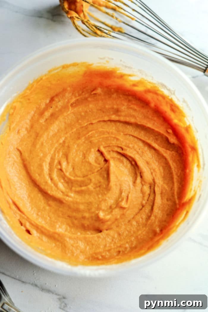 Thick, orange pumpkin muffin batter in a mixing bowl, ready to be scooped.