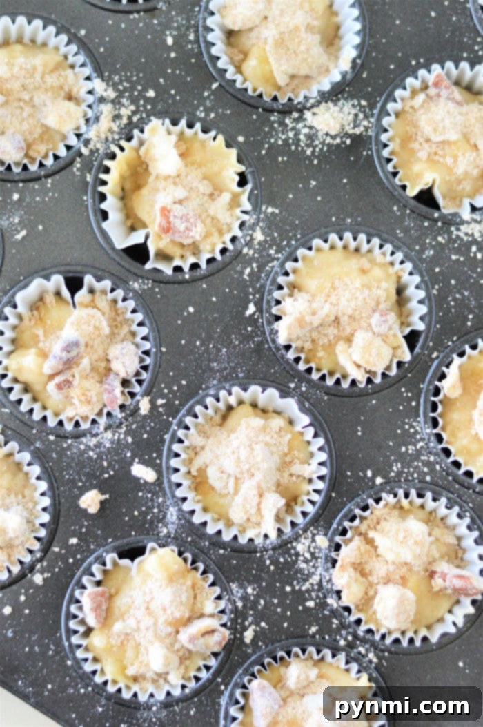 Golden Banana Bites 4 A muffin tray brimming with batter for mini muffins, crowned with streusel toppings, ready to bake.