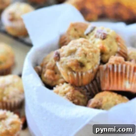A bowl of mini banana nut muffins lined with a white napkin, with more delicious mini banana muffins and ripe bananas in the background.