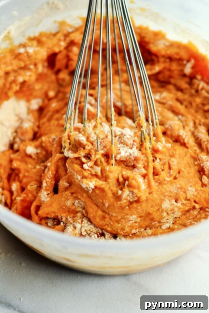 Close-up of freshly mixed homemade pumpkin muffin batter in a white bowl, ready for baking, highlighting its rich orange color.