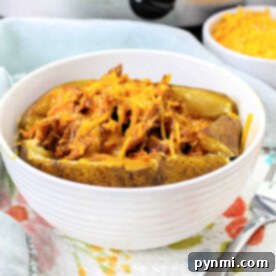A pulled pork baked potato topped with shredded chicken and melted cheese in a white bowl.