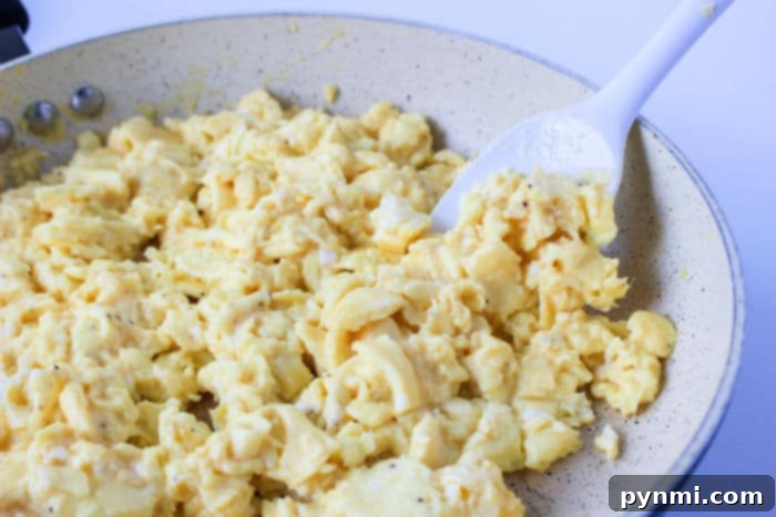 Crispy Ninja Foodi Air Fryer Breakfast Burritos 5 Scrambled eggs sizzle in a frying pan, a white spatula stirring them to perfection—a morning symphony for the perfect breakfast burrito.