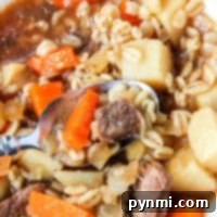 Hearty beef and barley stew with carrots and potatoes in a white bowl, slow-cooked to perfection in a crockpot.