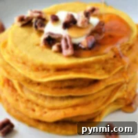 A stack of delicious pumpkin pancakes made with Bisquick, generously topped with butter, crunchy pecans, and a luscious syrup drizzle, presented invitingly on a plate.
