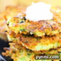 Three crispy zucchini corn fritters topped with a dollop of sour cream rest elegantly on a dark plate.
