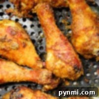 Crispy fried chicken drumsticks cooked to perfection in an air fryer, nestled in a perforated metal pan for ultimate crispiness without flour.