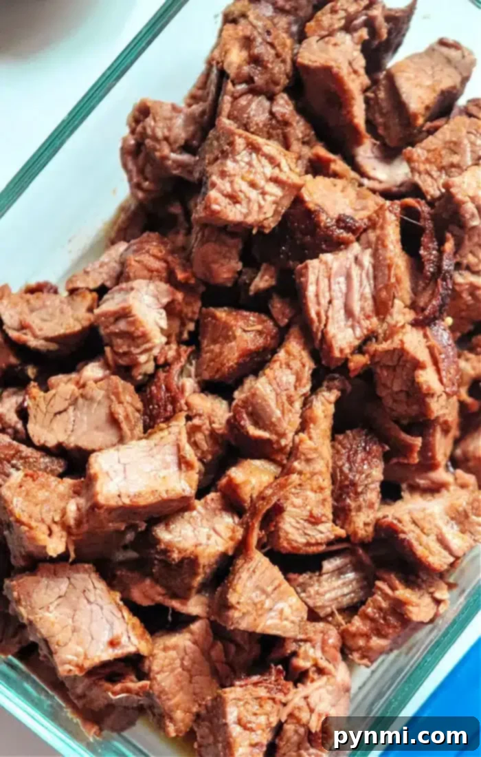 Perfectly Tender Air Fryer Brisket 7 A clear glass container filled with many pieces of cooked, cubed beef brisket, likely prepared in an air fryer. The meat appears browned and slightly crispy on some edges, perfect for enjoying immediately or saving for delicious leftover meals.