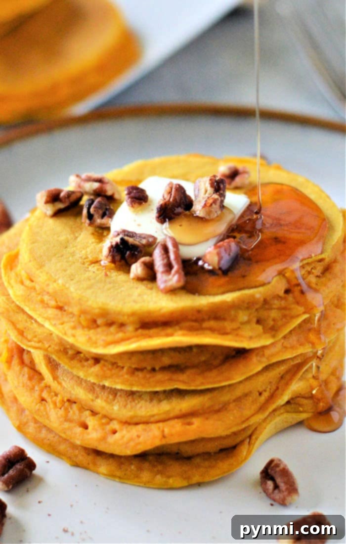 Effortless Bisquick Creations 3 A beautifully stacked tower of pumpkin pancakes made with Bisquick, garnished with a pat of melting butter, crunchy pecans, and a generous drizzle of golden syrup.