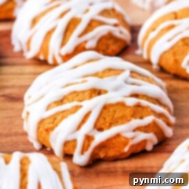Iced pumpkin cookies drizzled with white icing are artfully arranged on a rustic wooden surface.
