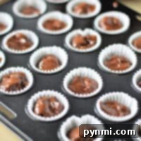 Mini chocolate cupcakes in white liners, ready for baking, fill the muffin tray with a luscious batter, promising a delightful treat.