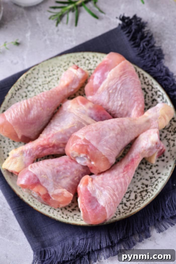 Raw chicken drumsticks on a speckled plate, ready to be seasoned after learning how to defrost chicken in the microwave, rest on a dark fabric napkin.
