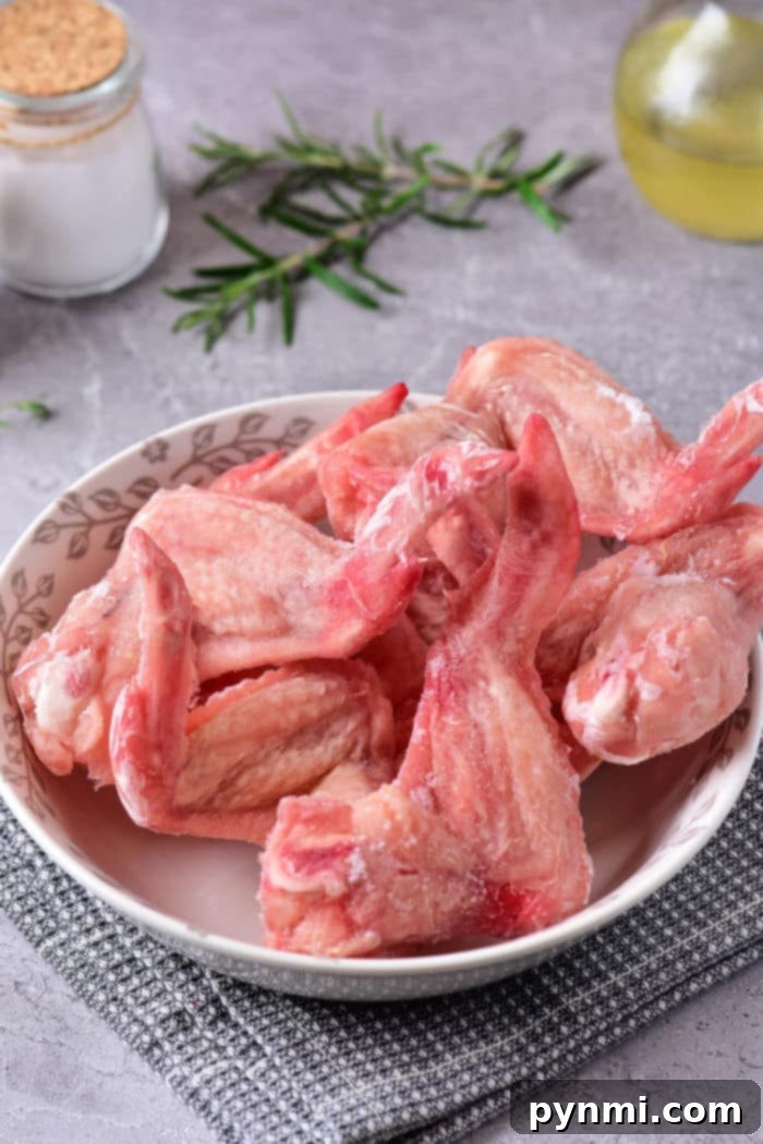 A bowl of raw chicken wings sits on a gray kitchen cloth adorned with fresh rosemary, oil, and a jar of salt in the background. Discover how to defrost chicken in the microwave to prepare your feast quickly and efficiently.