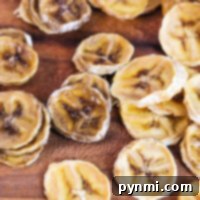 A close-up of sliced banana chips, expertly dehydrated, scattered on a rustic wooden surface.