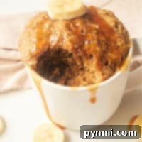 Banana Bread in a Mug: A mouthwatering banana mug cake with a bite taken, topped with fresh banana slices and drizzled syrup, all on a pristine white surface.