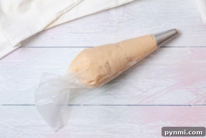 A piping bag filled with churro dough lies invitingly on a white wooden surface, ready to make air fryer chocolate-filled churros.