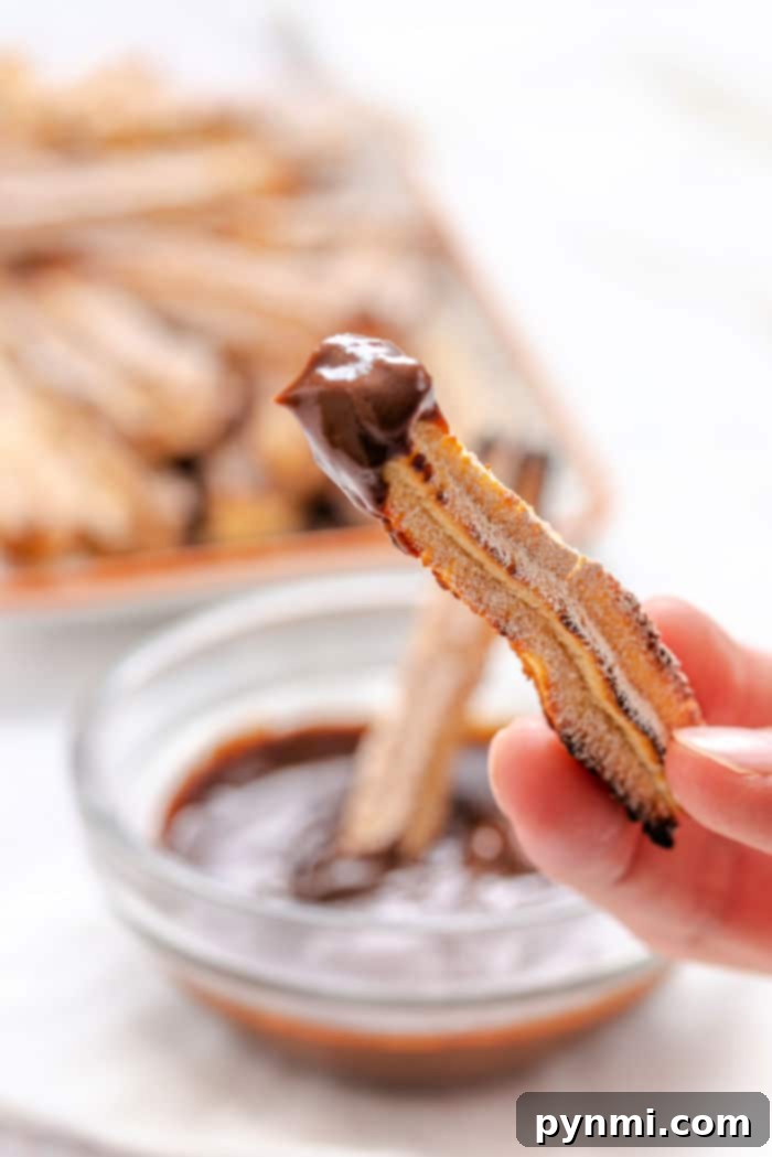 Oven-baked churros arranged on a baking sheet, golden and ready for filling.