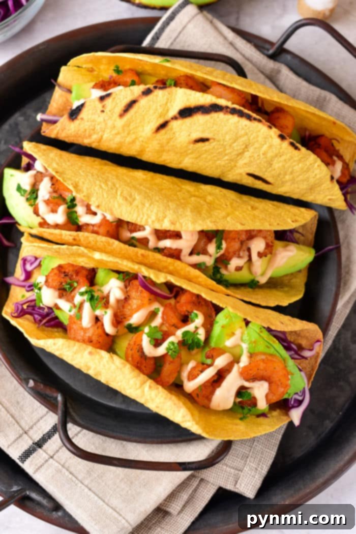 Three shrimp tacos with avocado, purple cabbage, and sauce nestled in air-fried corn tortilla shells on a black platter.