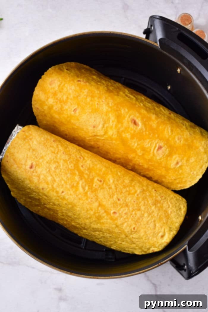 Two yellow tortilla shells wrapped around delicious fillings, nestled side by side in a black cooking pot, reminiscent of taco shells prepared perfectly in an air fryer.
